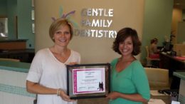 Two women holding a framed certificate in front of a sign.