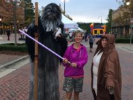 A woman holding a purple wand standing next to a person dressed as chewbacca.